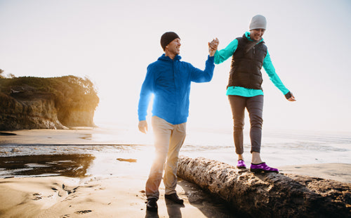 active couple climbing rocks alongside a coastal beach