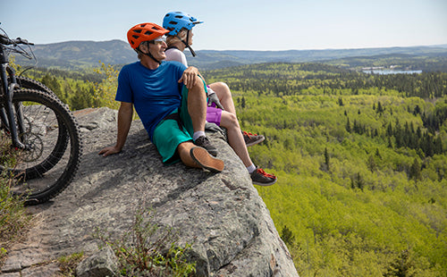 two active bikers sitting on top of a mountain smiling